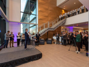 Crowd in two-story modern lobby listens to a speaker on the stage.