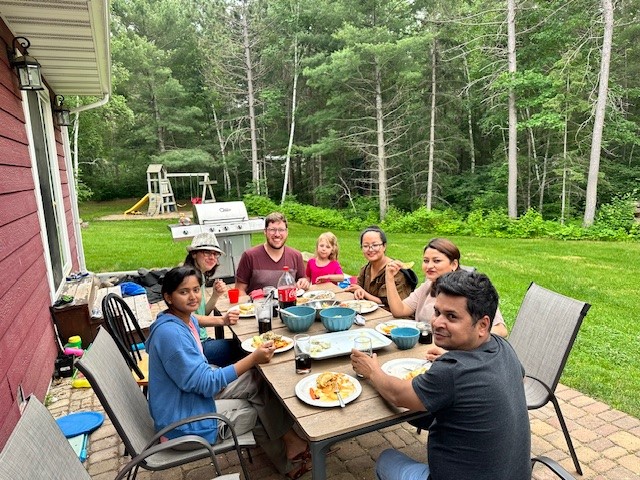 Friends of different nationalities share a picnic dinner in a wooded backyard.