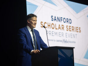 Doctor speaks at a podium with a screen behind him that says "Sanford Scholar Series Premier Event."