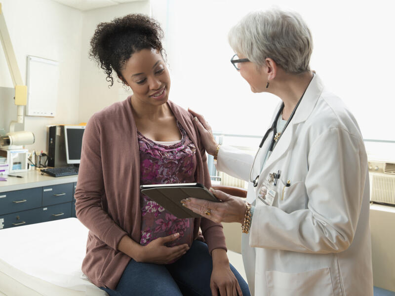 Gynecologist with digital tablet comforting pregnant patient