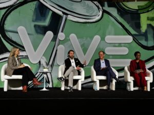 Panel of four professionals seated on stage against green and black backdrop with the word "ViVE."