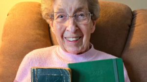 100-year-old woman smiles holding a very old diary next to a new diary