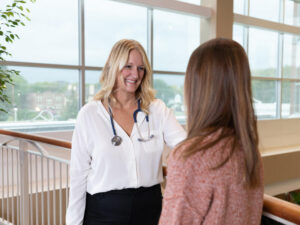 A smiling doctor with a stethoscope reassures a patient in the lobby of a hospital.