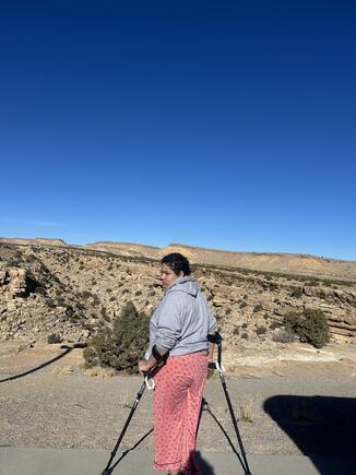Young woman with crutches stands facing desert landscape.