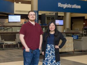Professional man and woman from switchboard and IT support staff smile in front of hospital registration desk.