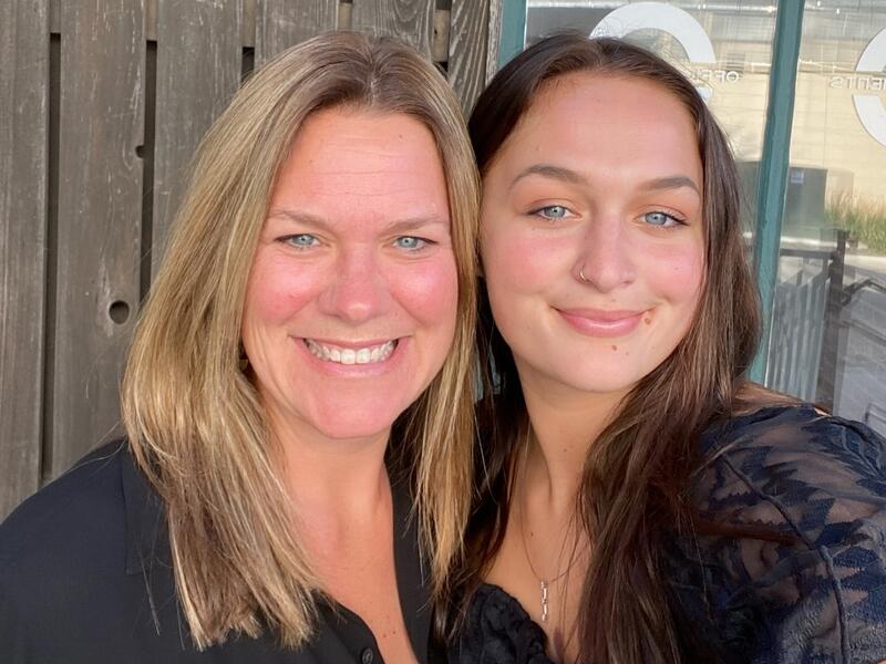 Mother and young adult daughter smile together.