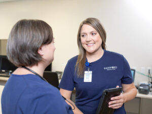 Two nurses talk at a nurses station.