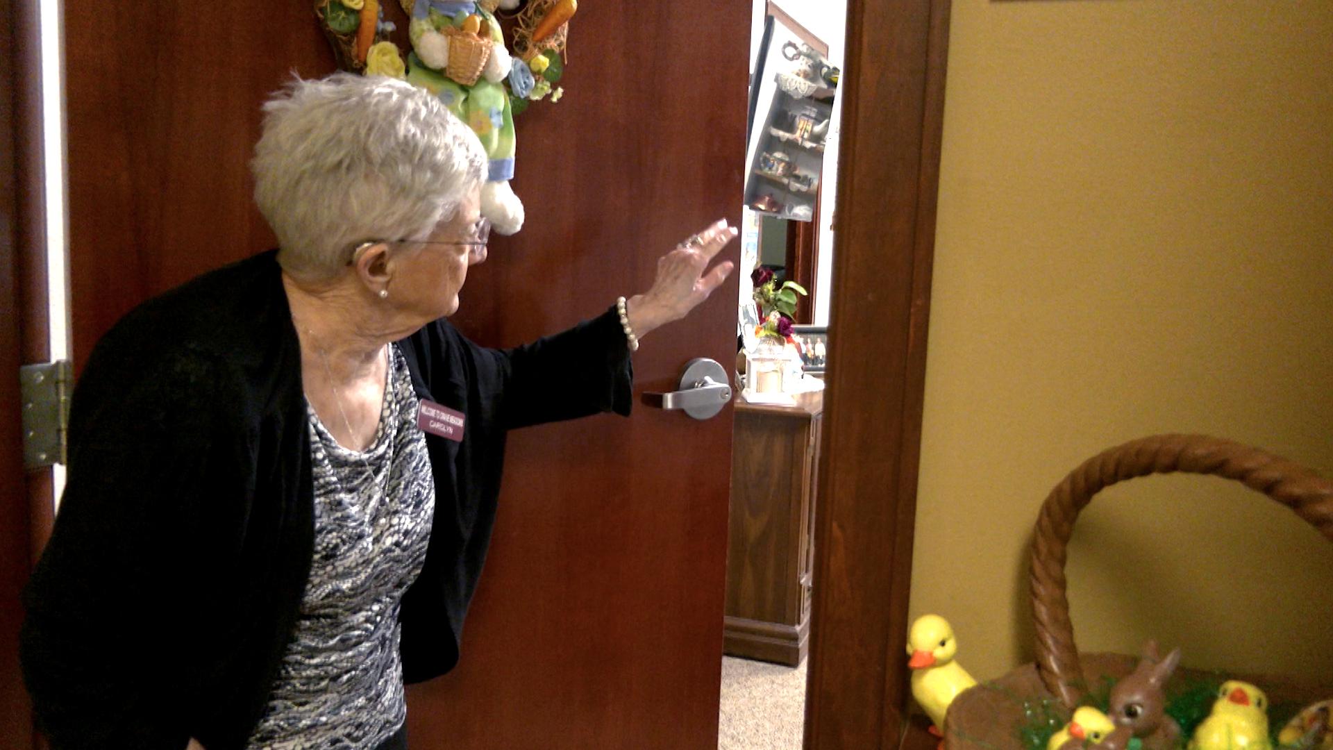Senior woman waves though an open door from left.