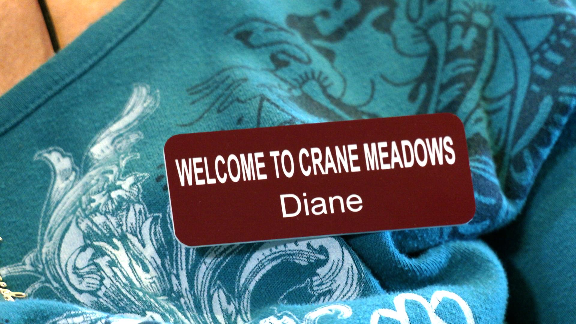 Closeup of red and white nametag: "Welcome to Crane Meadows. Diane"