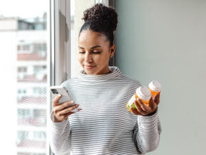 A young woman standing by the window and researching about the medicine online.