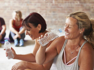 Two women laughing and drinking from water bottles in the gym