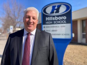Superintendent participating in BeHEARD program stands in front of school sign
