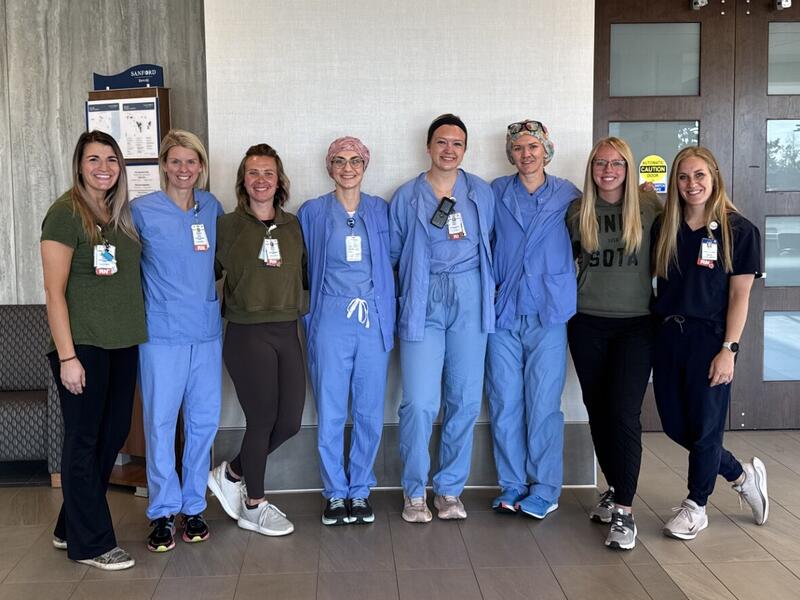 group of 8 nurses standing in black and blue scrubs.