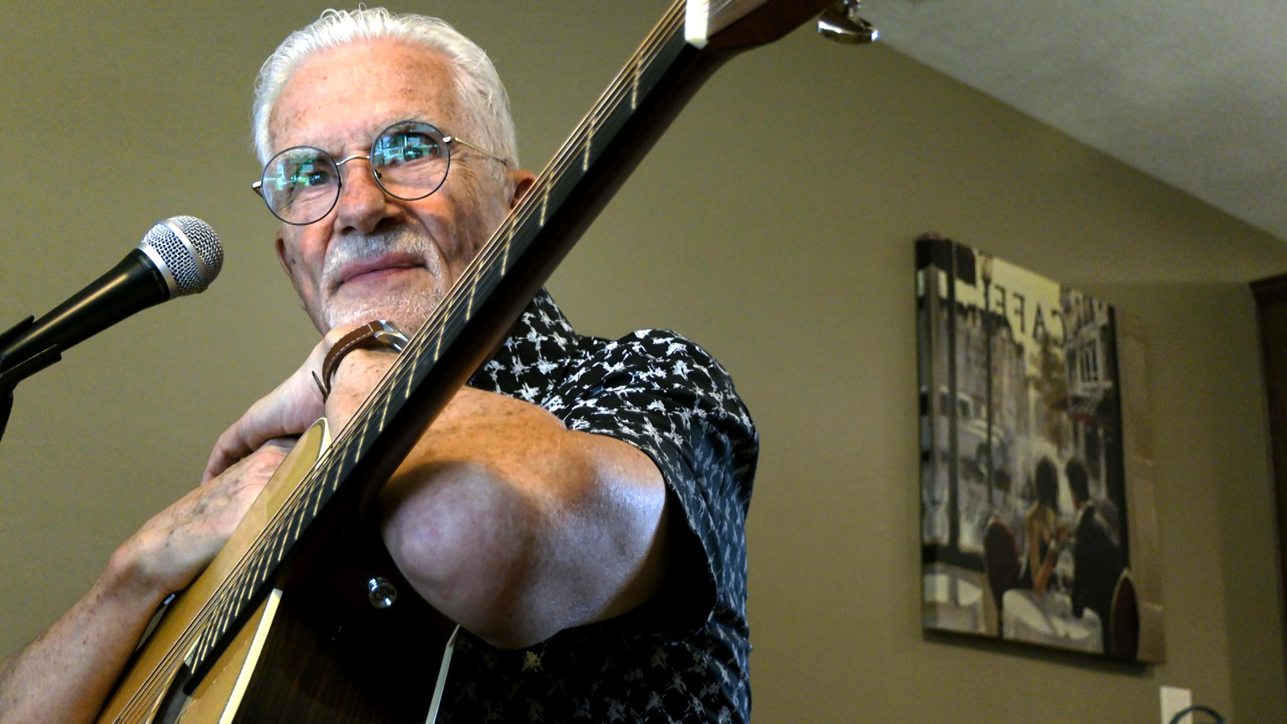 Senior man leans on his acoustic guitar.