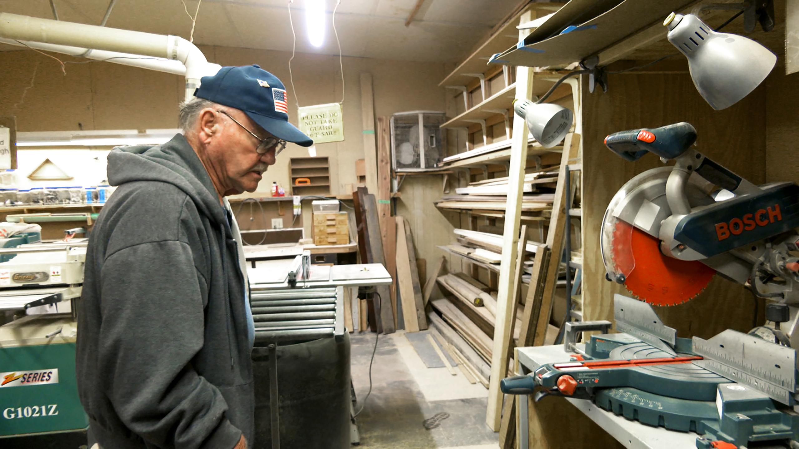Senior man inspects a tool bench in a woodworking shop.