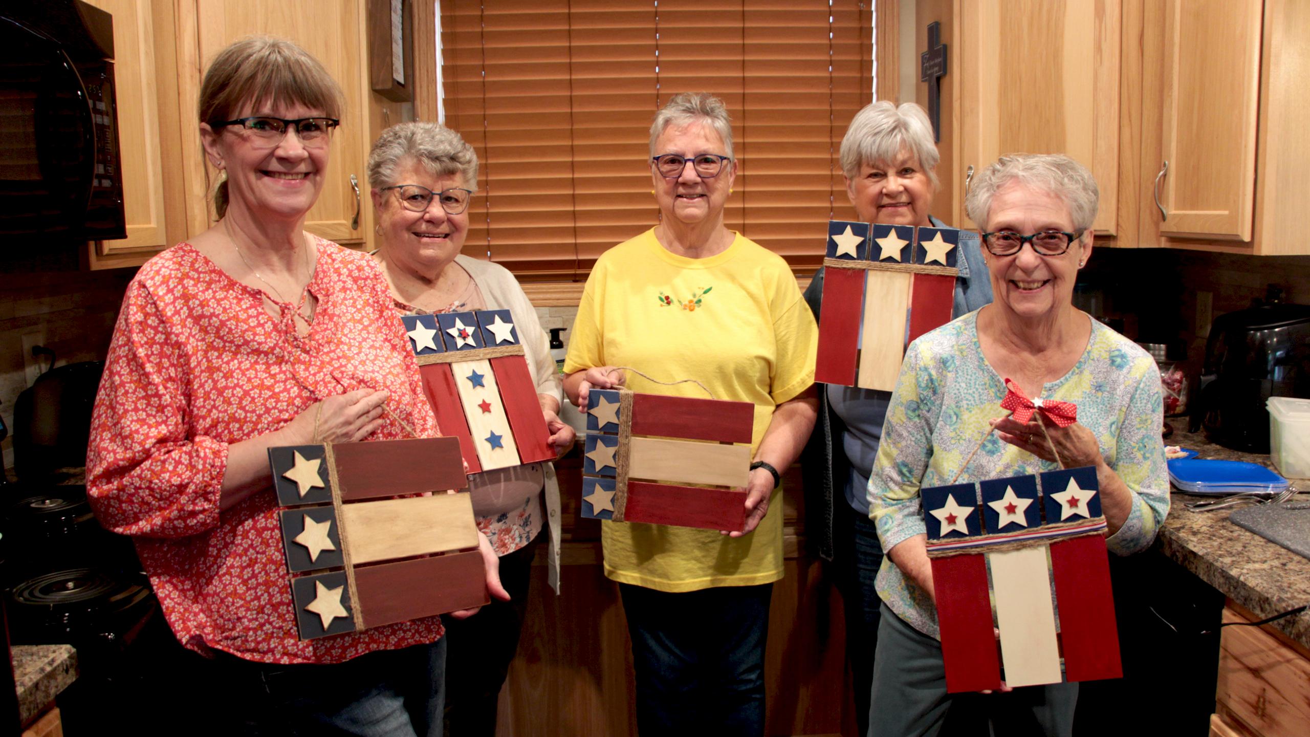 Five senior women hold their red, white and blue wooden craft projects.