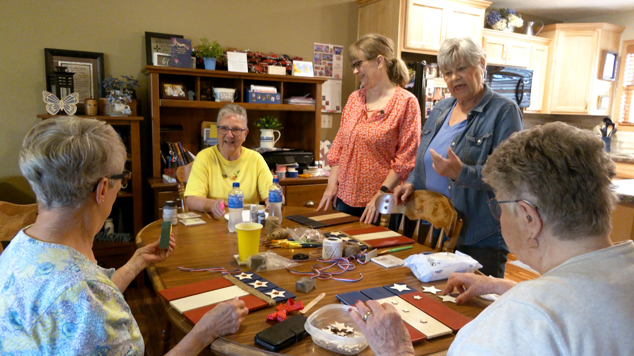 Senior women talk around a kitchen table while doing crafts.