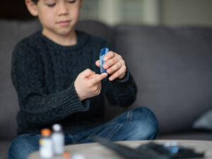 A boy is sitting in the living room. He is checking his blood sugar level because he is diabetic.