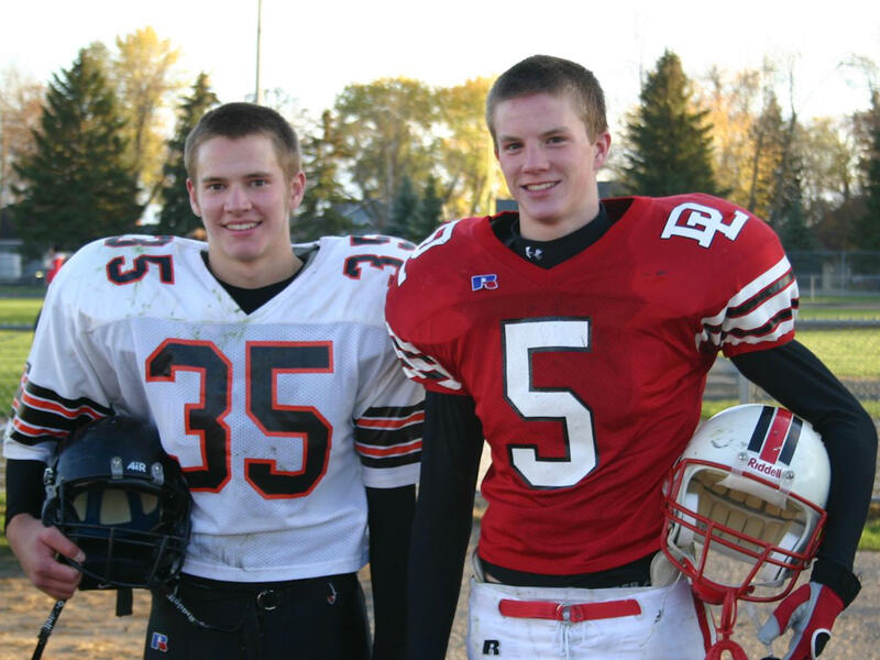 Two high school football players from different teams pose in their uniforms.