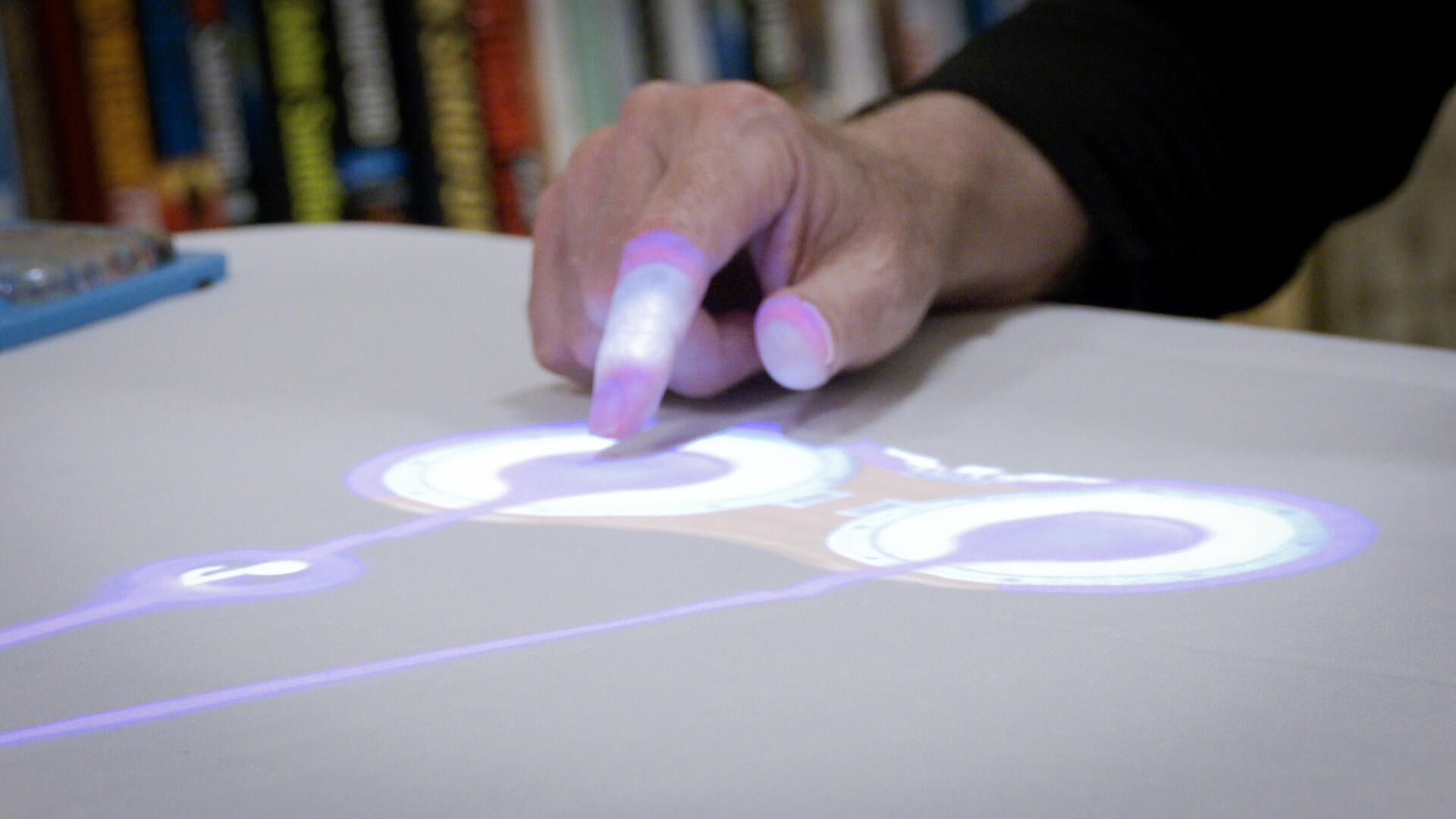 Closeup of a senior man's hand as he taps images of circles and musical notes on a table.