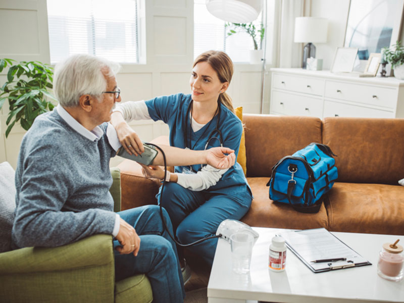 Nurse visiting mature patient at home. She is measuring blood pressure to patient at his living room.