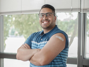 Happy young man shows off his upper arm bandage where he just got a vaccination.