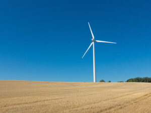 Wind turbine stands in a harvested farm field against a blue sky.
