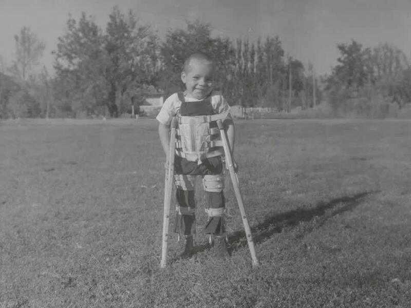Young boy stands outside in leg and body braces with help of crutches.