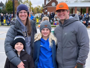 Mom, Dad and two kids in winter gear wait for a parade to start.