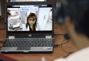 Telehealth doctor on a laptop computer screen speaking with a patient in the foreground.