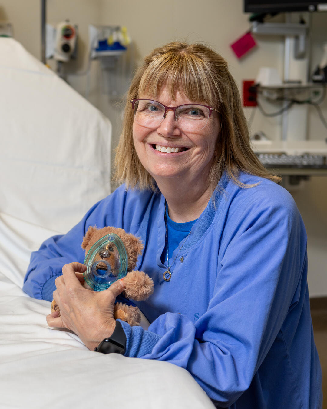 Child life specialist Lorri Ferguson holds a stuffed animal at a hospital bedside.