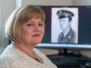 Woman smiles next to black and white photo of her dad in military uniform.