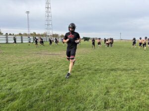 Football practice in a rural field shows one player running in front.