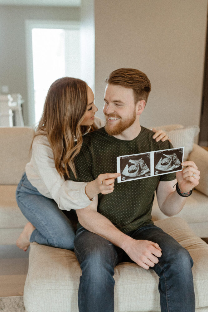 Young happy couple holds up two ultrasound photos for pregnancy announcement.