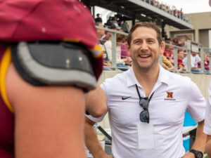 Man in a Northern State polo shirt laughs with a football player on the sidelines.