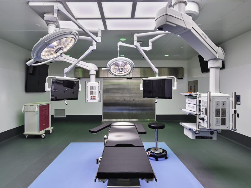 Operating room with patient table at center, and attached to ceiling are computer monitors, lights and the arm of an intraoperative MRI machine.
