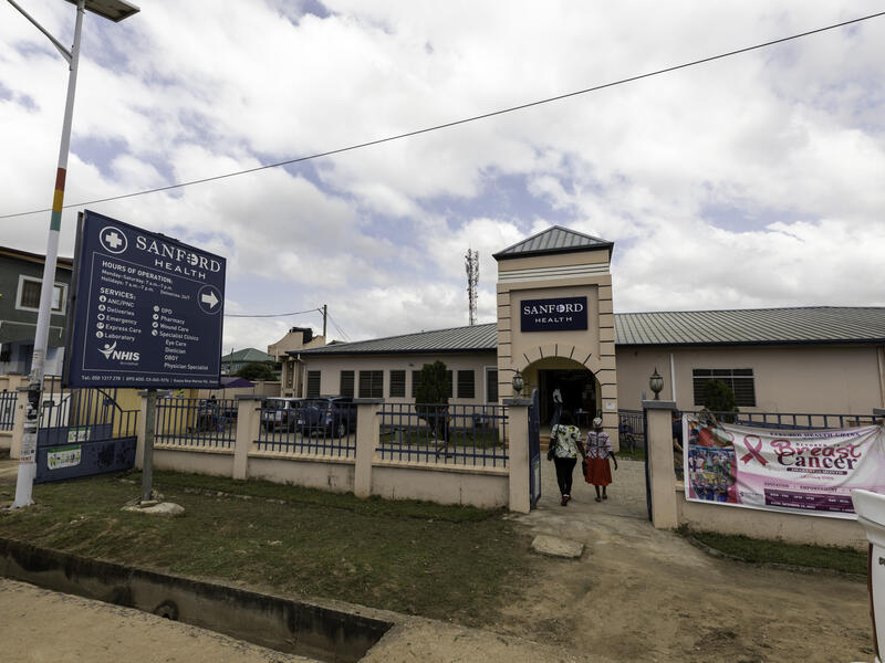 Street view of Sanford clinic with two women entering the gated grounds in Ghana, West Africa.
