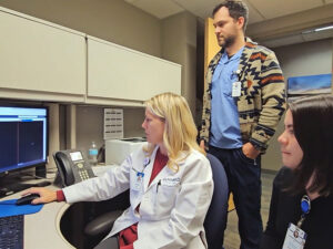 Two Sanford Health workers watch a doctor at her computer leading a medical education session.