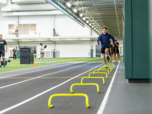 Young athlete runs on a track lined with low agility bars as obstacles.