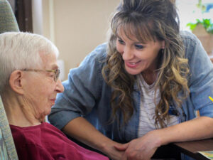 Younger nurse smiles with older adult nursing home resident.