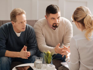 Two serious men speak with a therapist.