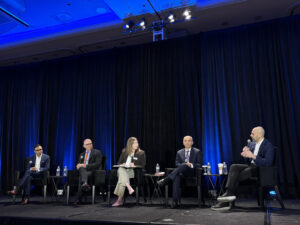 Five businesspeople sit on conference stage.