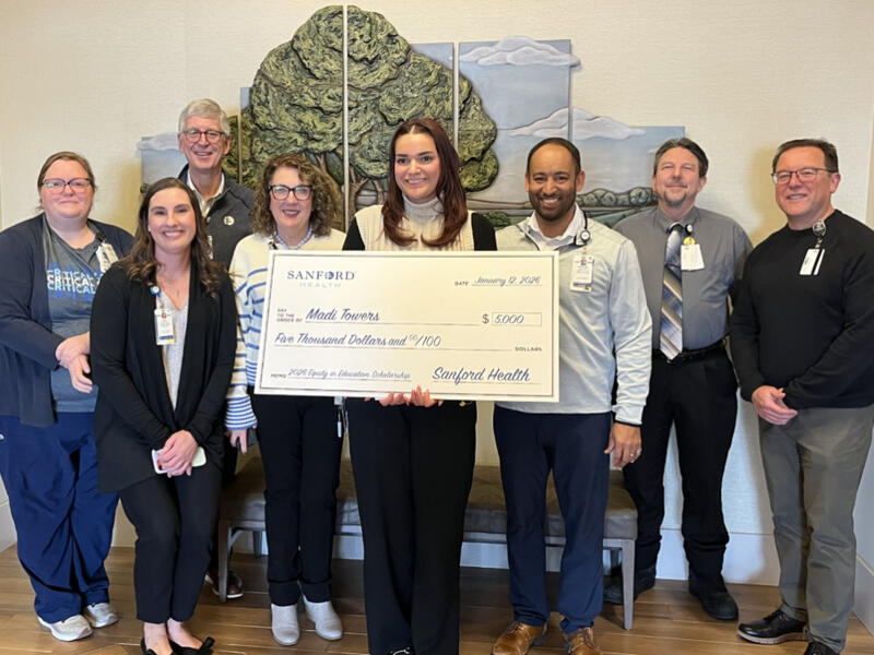 Group of people hold a giant check for the Sanford Equity in Education Scholarship in front of a tree mural.