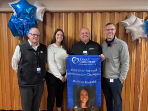 Four businesspeople hold a banner celebrating Madison Kinkaid, Ever Forward Administrator Champion.