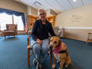 Older woman seated with dog at her side.