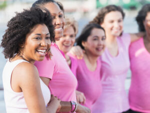 Mothers and daughters wearing pink in support of breast cancer awareness. They are standing side by side, smiling and laughing.
