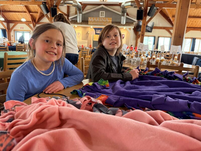 Two girls at a table making a fuzzy blanket.