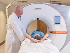 man in lab coat stands over women patient laying flat by CT scanner