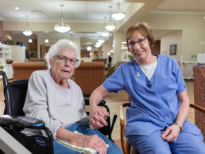 A nurse holds hands with a senior woman using a wheelchair.