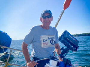 Happy senior man holds the steering wheel of a sailboat on a lake.